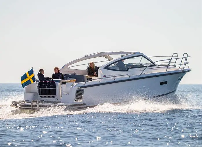 A white motorboat speeds across the water, carrying three people and displaying a Swedish flag.